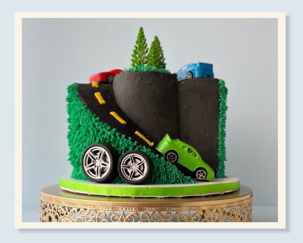 car cake design process featuring a winding road and toy cars on buttercream grass