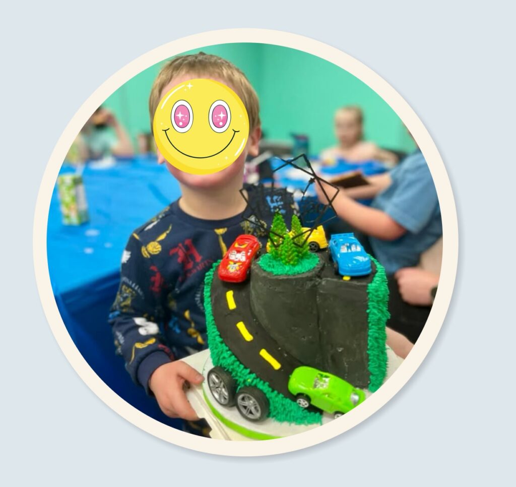 Child holding custom car-themed birthday cake with road design and toy cars